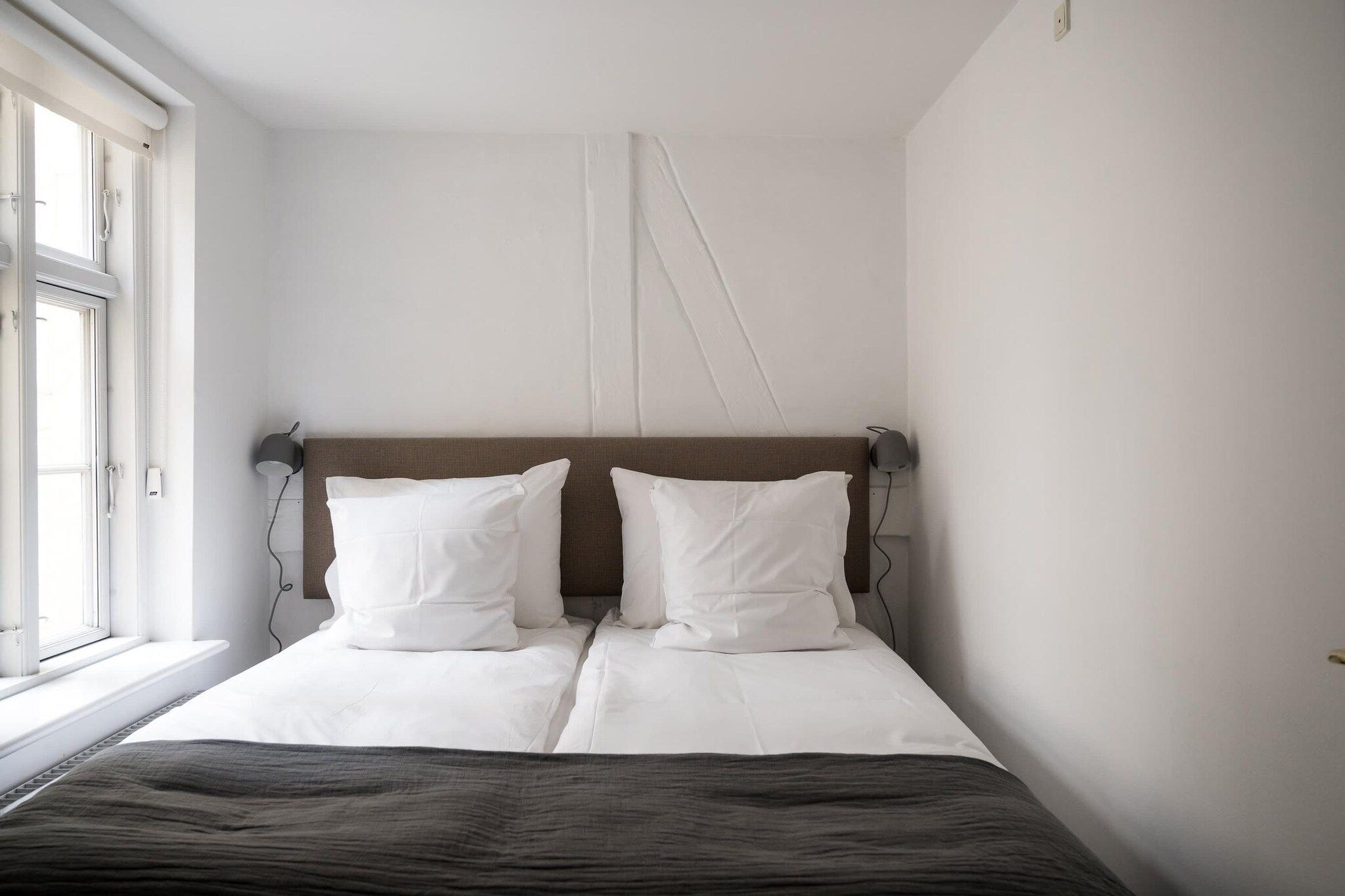 A bedroom with a bed, two bedside lamps, a window, and a wall-mounted light fixture.