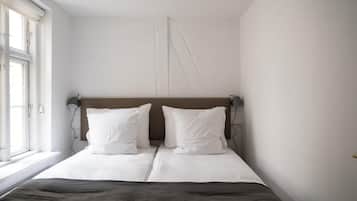A bedroom with a bed, two bedside lamps, a window, and a wall-mounted light fixture.