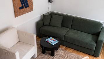 A living room with a green sofa, a beige armchair, and a small black table with a book.