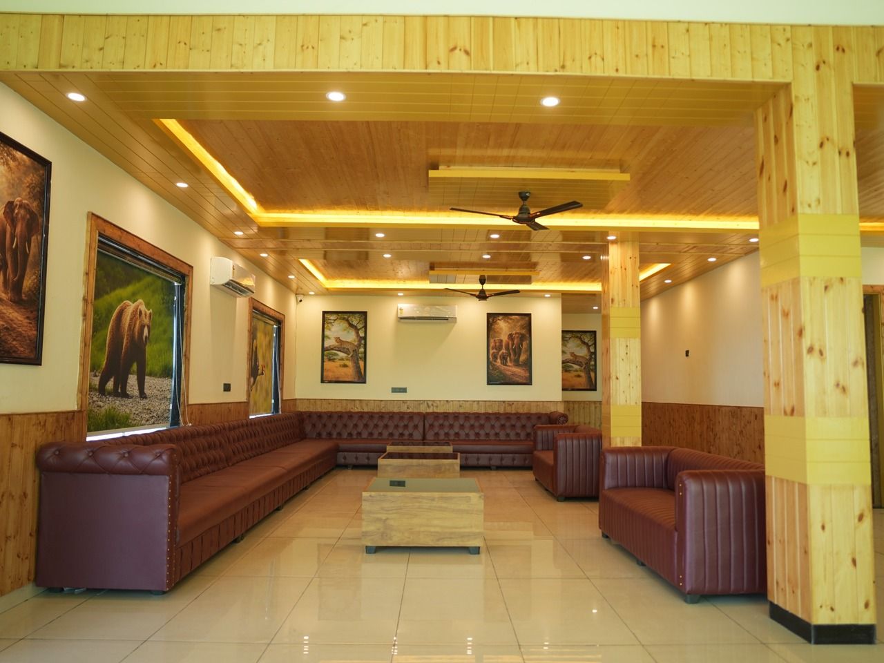 Um hall amplo com um extenso sofá de couro marrom, uma mesa de centro e um ventilador de teto.