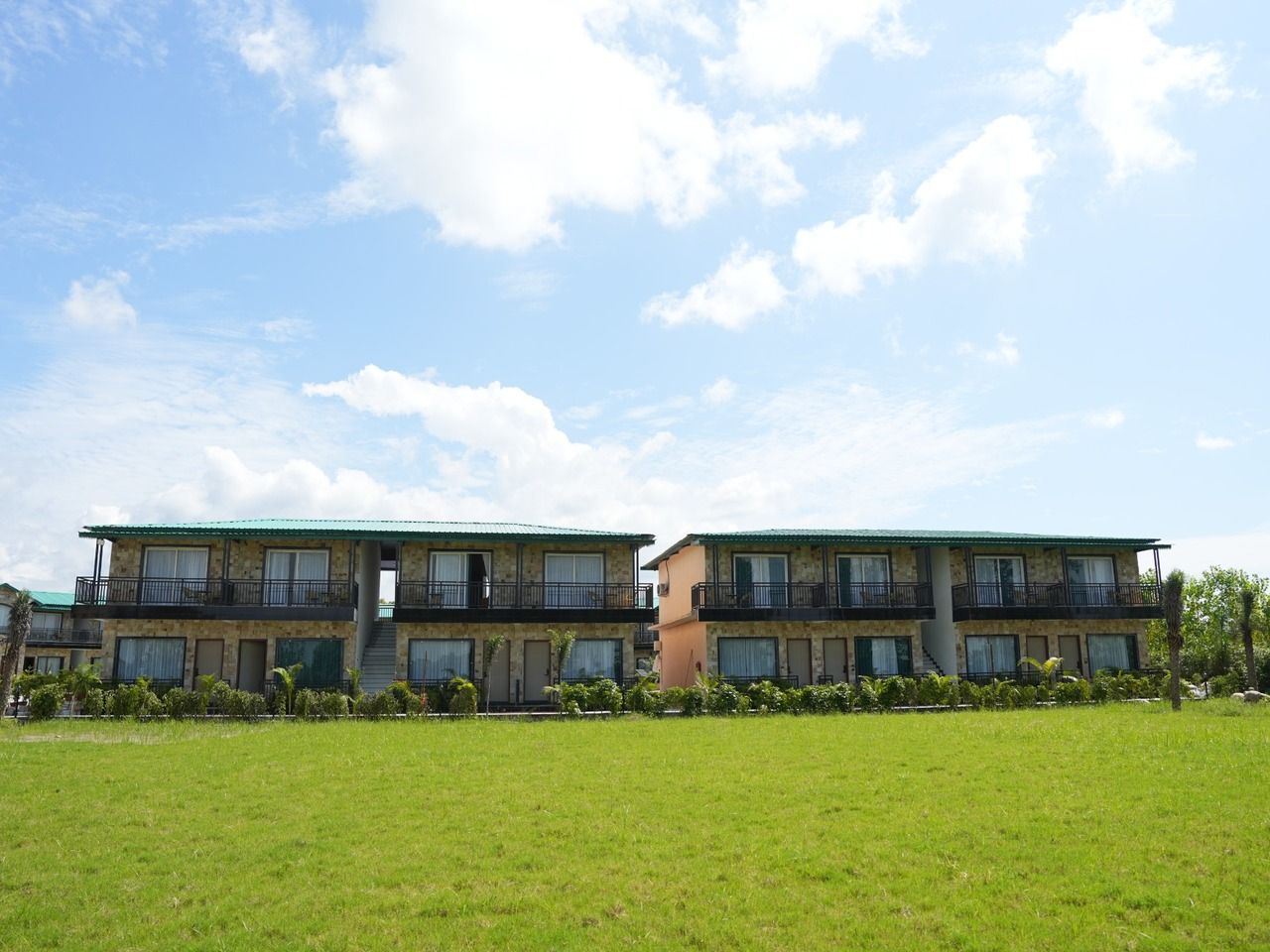 A two-story building with balconies, a flat roof, and a grassy lawn in front.