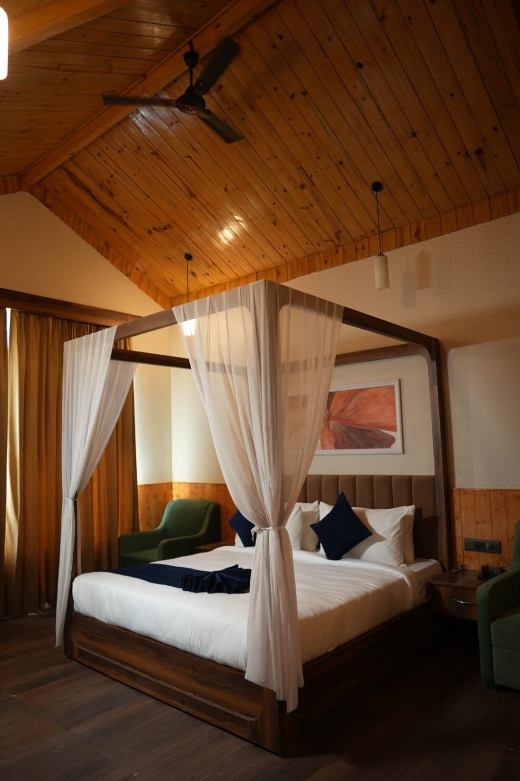 A four-poster bed with sheer curtains, a wooden ceiling, and a green chair.