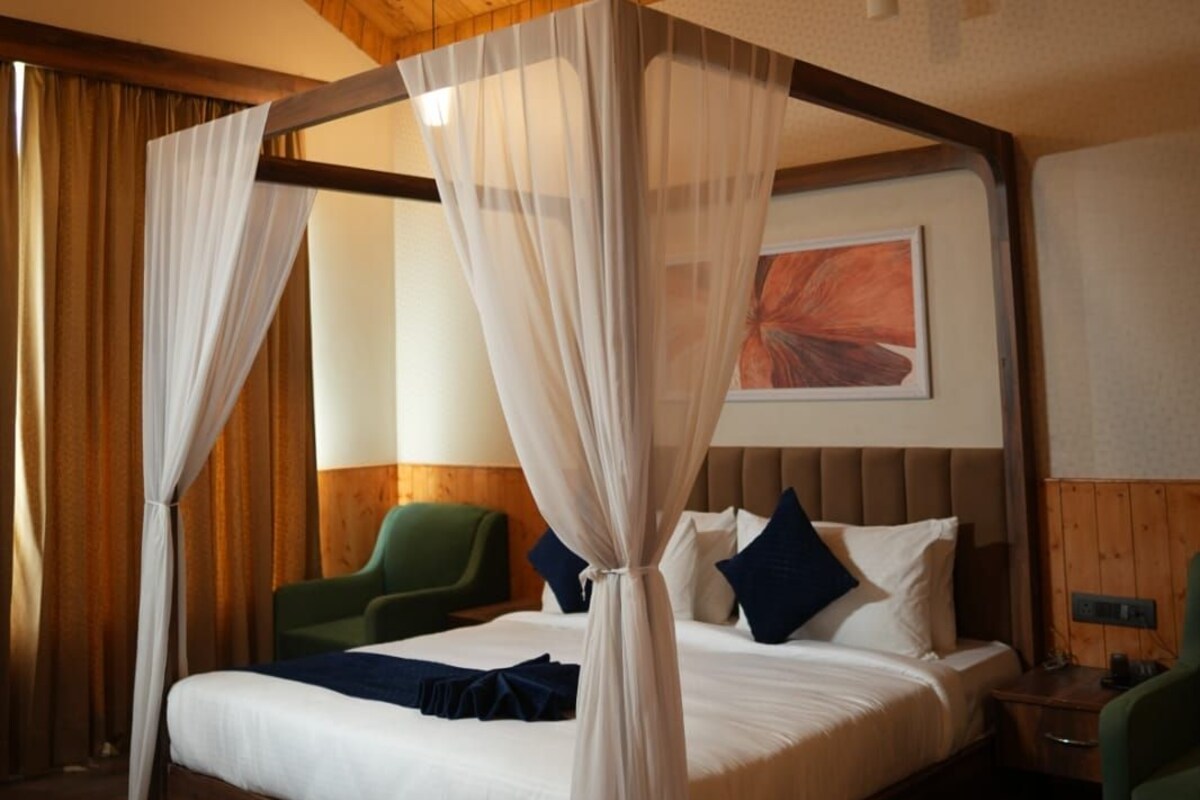 A four-poster bed with sheer curtains, a wooden ceiling, and a green chair.