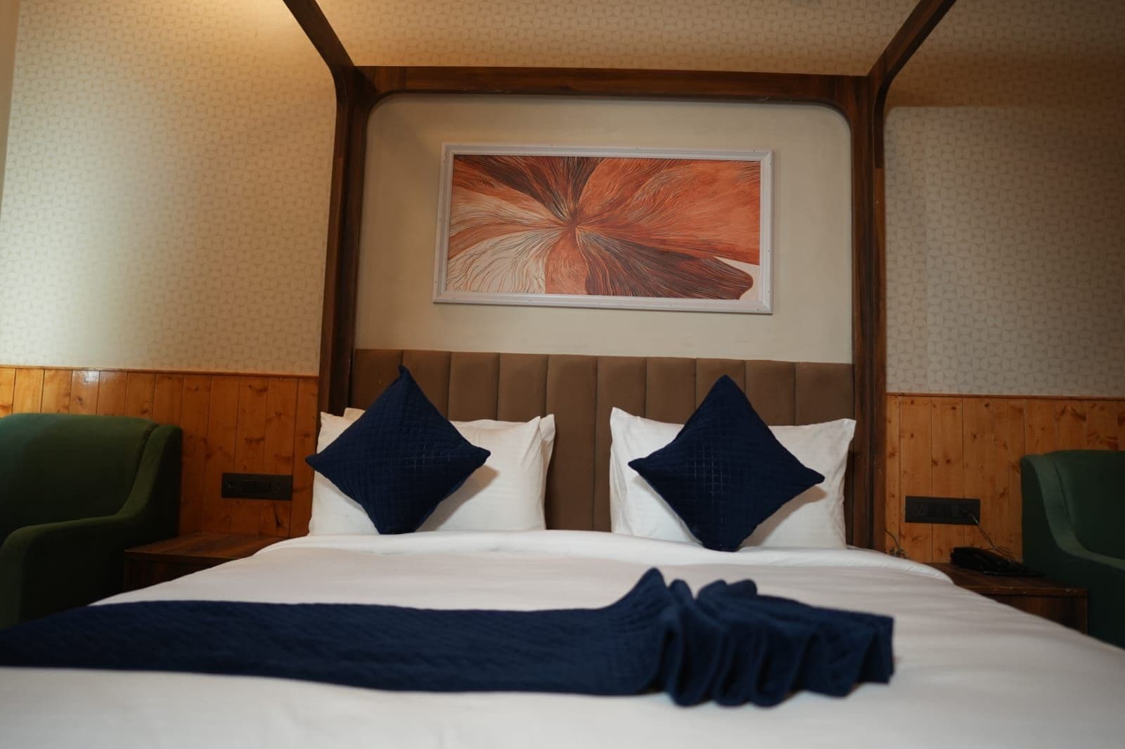 A hotel room with a bed, two pillows, a blanket, and a painting on the wall.