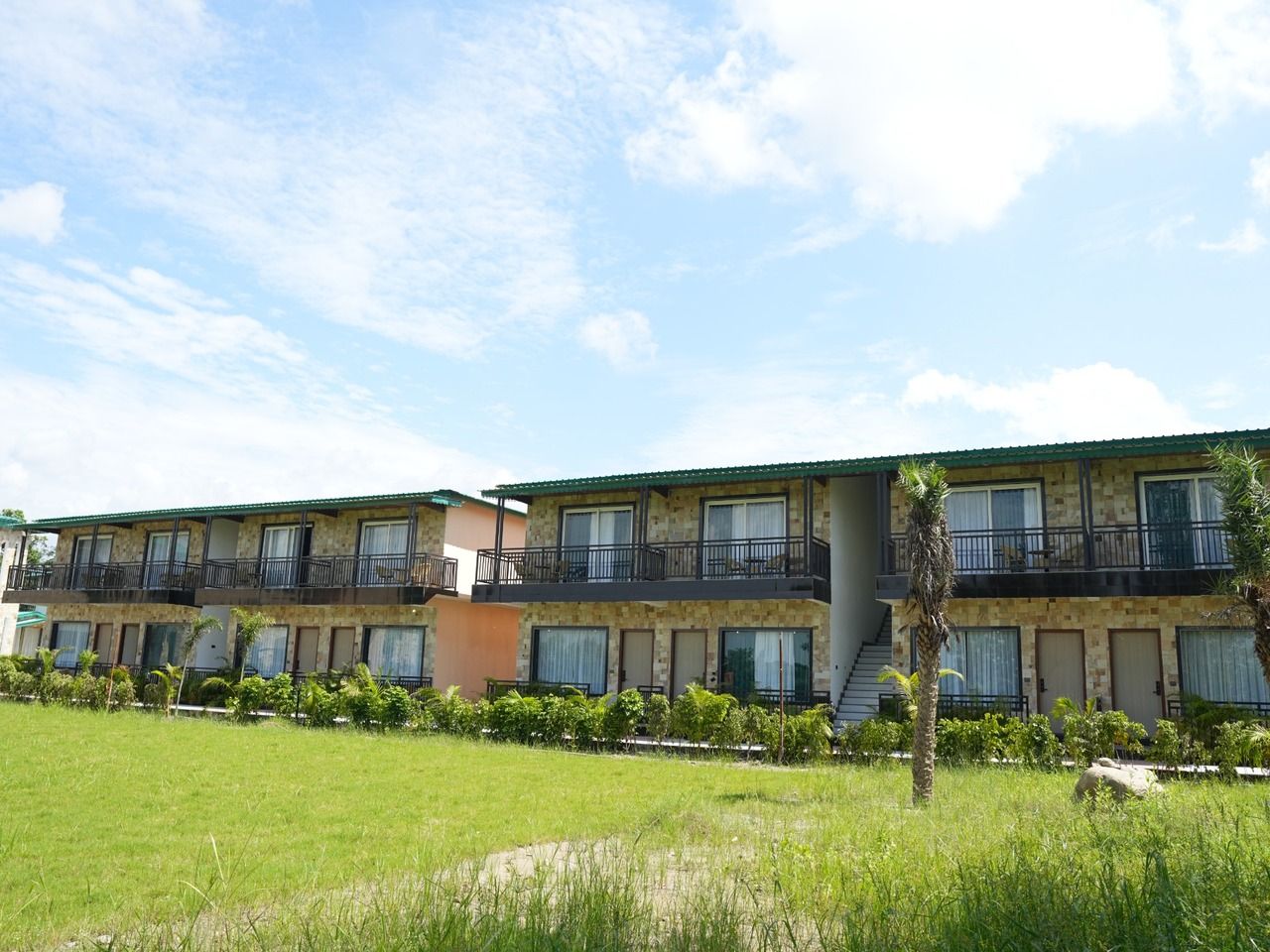 A multi-story hotel with balconies, a flat roof, and a grassy lawn.