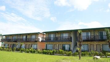 A multi-story hotel with balconies, a flat roof, and a grassy lawn.
