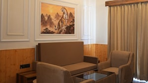 A room with a wooden ceiling, a sofa, a chair, a painting, and a window with curtains.