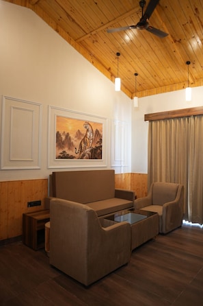 A room with a wooden ceiling, a sofa, a chair, a painting, and a window with curtains. - Onyxx Nature Resort (Ramnagar)
