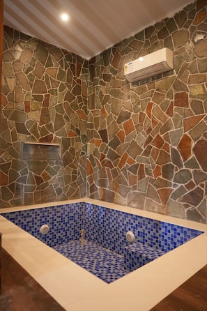 A stone-walled bathroom with a blue-tiled bathtub.