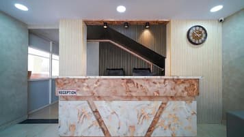 Balcão de recepção com design em mármore, um relógio e uma escadaria que leva a um andar superior.