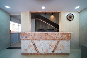 Un taulell de recepció amb disseny de marbre, un rellotge i una escala que condueix a un nivell superior.