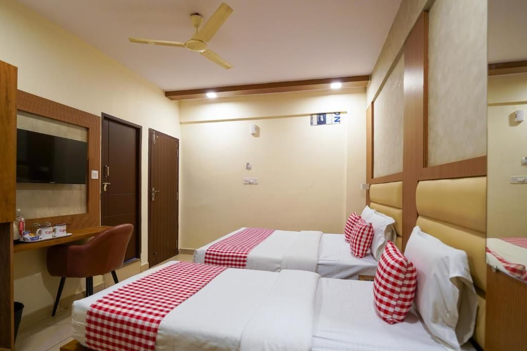 Quarto de hotel com duas camas, uma escrivaninha, uma cadeira, uma televisão e um ventilador de teto.