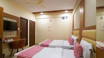 Quarto de hotel com duas camas, uma escrivaninha, uma cadeira, uma televisão e um ventilador de teto.