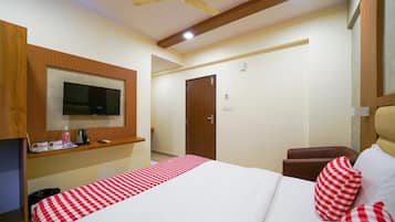Quarto de hotel com cama, televisão na parede, ventilador de teto e armário de madeira.