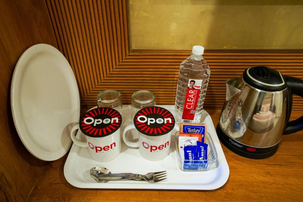 Uma bandeja com duas canecas da marca 'Open', uma garrafa de água, uma caixa de chá Tetley, uma cafeteira e uma colher.