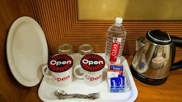 Uma bandeja com duas canecas da marca 'Open', uma garrafa de água, uma caixa de chá Tetley, uma cafeteira e uma colher.