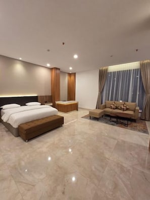 A modern bedroom with a large bed, a sofa, and a small table. - Comforta Suites Hotel (Palembang)