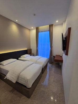 A hotel room with two beds, a desk, and a TV. - Comforta Suites Hotel (Palembang)