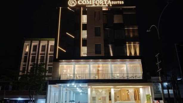 Un hotel llamado 'COMFORTA SUITES' con una fachada moderna, ventanas amplias y una entrada bien iluminada.