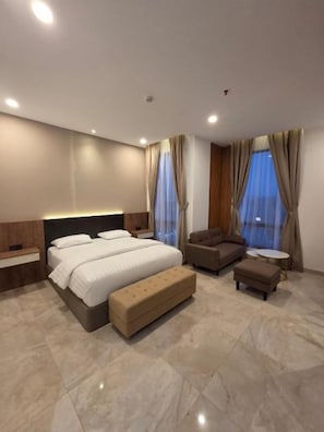 A modern hotel room with a large bed, a sofa, a small table, and a bench. - Comforta Suites Hotel (Palembang)