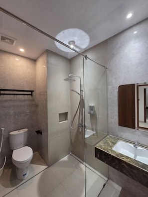 A modern bathroom with a glass-enclosed shower, a toilet, and a sink with a marble countertop. - Comforta Suites Hotel (Palembang)