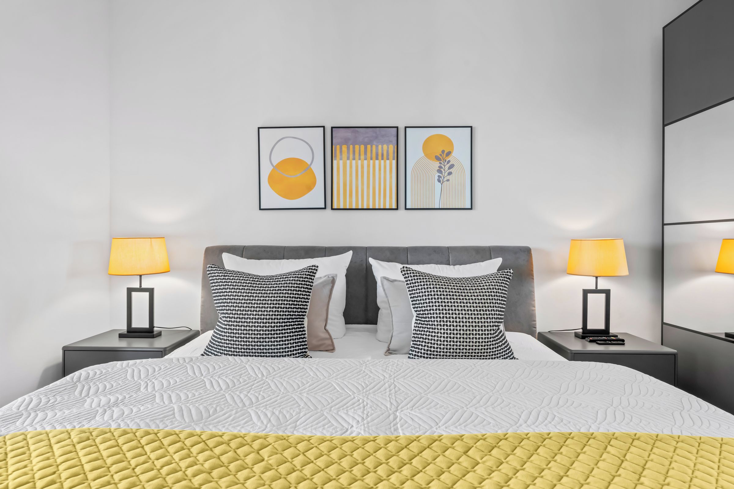 Une chambre d’hôtel moderne avec un grand lit, deux tables de chevet et un téléviseur fixé au mur.