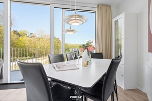 Een moderne eethoek met een witte tafel, zwarte stoelen en een glazen vaas met bloemen.