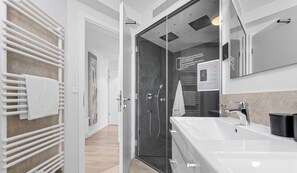 Een moderne badkamer met een glazen douchecabine, een witte wastafel en een handdoekhouder.