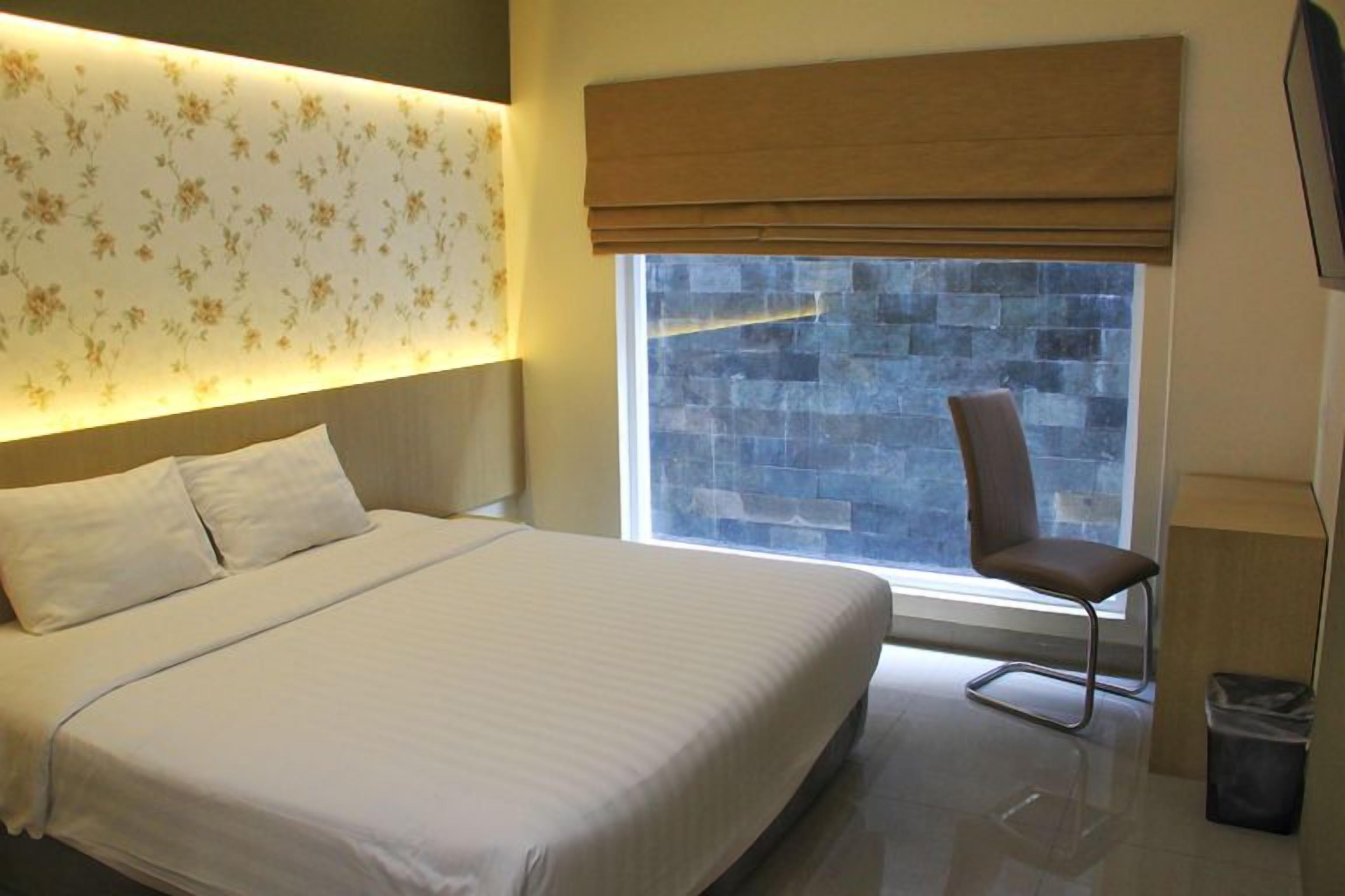 Habitació d'hotel amb un llit gran, una cadira, una finestra amb vista a una paret de pedra i una televisió penjada a la paret.