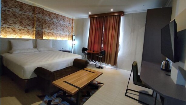 Une chambre d’hôtel avec un grand lit, un bureau, une chaise, une télévision et une fenêtre avec des rideaux.