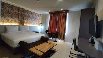 A hotel room with a large bed, a desk, a chair, a television, and a window with curtains.