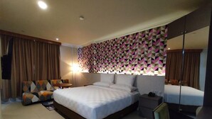 Une chambre d’hôtel avec un grand lit, un coin salon comprenant une chaise et une table, une table de chevet avec une lampe et un miroir.