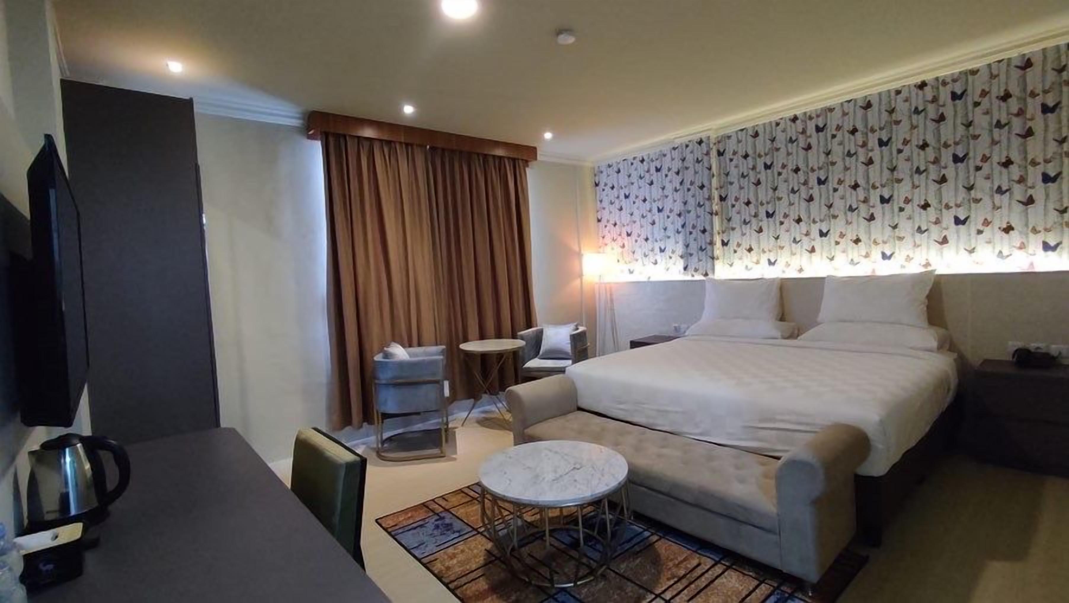 A hotel room with a bed, a desk, a chair, a small round table, and a television.