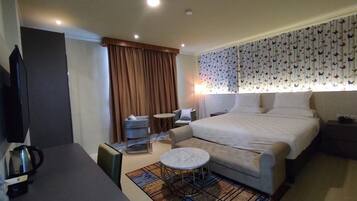 A hotel room with a bed, a desk, a chair, a small round table, and a television.