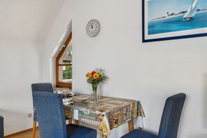 A dining area with a table set for two, a clock on the wall, and a painting of a sailboat. - Reutemann Guesthouse WG2 - Cozy vacation rental in a quiet, central location (Nonnenhorn)