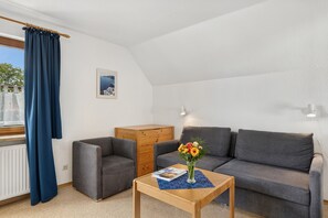 A cozy living room with a grey sofa, a wooden coffee table, and a blue curtain. - Reutemann Guesthouse WG2 - Cozy vacation rental in a quiet, central location (Nonnenhorn)