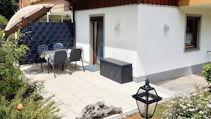 Eine Terrasse mit Tisch und Stühlen, ein Holzzaun und ein Gebäude mit einem Balkon.