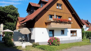 Ein zweigeschossiges Holzhaus mit einem geneigten Dach, einem Balkon mit Blumenkästen und einem gepflasterten Auffahrt.