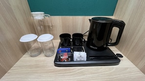 A coffee station with a black coffee maker, two black mugs, two empty glass cups, a tray with coffee pods, and a sugar packet. - Hotel Kawa Samarinda Japanese Style (Samarinda)