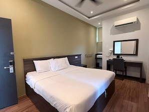 Habitación de hotel con una cama grande, un escritorio, una silla, un equipo de aire acondicionado y una puerta.