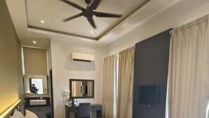 Une chambre d’hôtel avec un grand lit, un bureau, une chaise, un ventilateur de plafond et des rideaux.