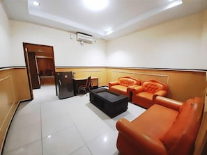 A hotel room with a sofa, a small table, a refrigerator, and a door leading to another room. - Hotel Grand Duta Syariah Palembang (Palembang)