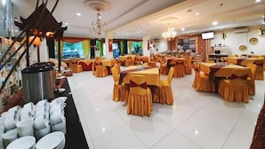 Un comedor amplio con múltiples mesas y sillas, un candelabro y una mesa de buffet con platos.