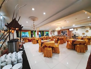 A spacious dining area with multiple tables and chairs, a chandelier, and a buffet line with dishes. - Hotel Grand Duta Syariah Palembang (Palembang)
