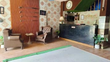 Zona de recepción con mostrador, un reloj y un cartel que indica 'The Hamlet' hotel.