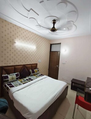 A bedroom with a bed, a ceiling fan, a wardrobe, and a desk. - The Hamlet Hotel (Noida)
