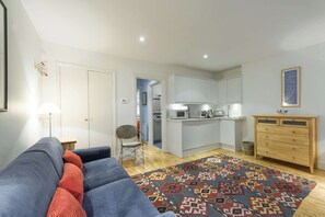 A modern living room with a sofa, a patterned rug, and a kitchen area with cabinets and a microwave. - Cosy 1-bed - Fitzrovia - Sleeps 3 (London)