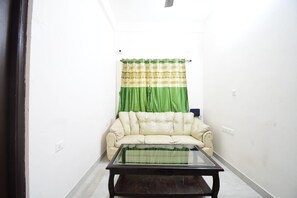 A room with a beige sofa, a glass-top coffee table, and green curtains. - Moon Residency Saltlake (Barasat)