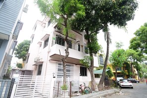 Un edificio residencial de varios pisos con entrada protegida por un portón, una bicicleta estacionada afuera y un coche aparcado en la calle.