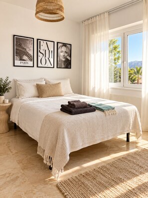 A bedroom with a large bed, a hanging light fixture, a window with curtains, and two framed pictures on the wall. - Stunning 4-Bedroom Villa | Private Pool & Ocean Views | Mijas Costa (Las Lagunas de Mijas)